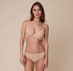 Gracie wearing the No-Show Thong in Beige, paired with a matching Base T-Shirt Bra. She poses with a soft smile, showcasing the thong’s flattering, seamless design.
