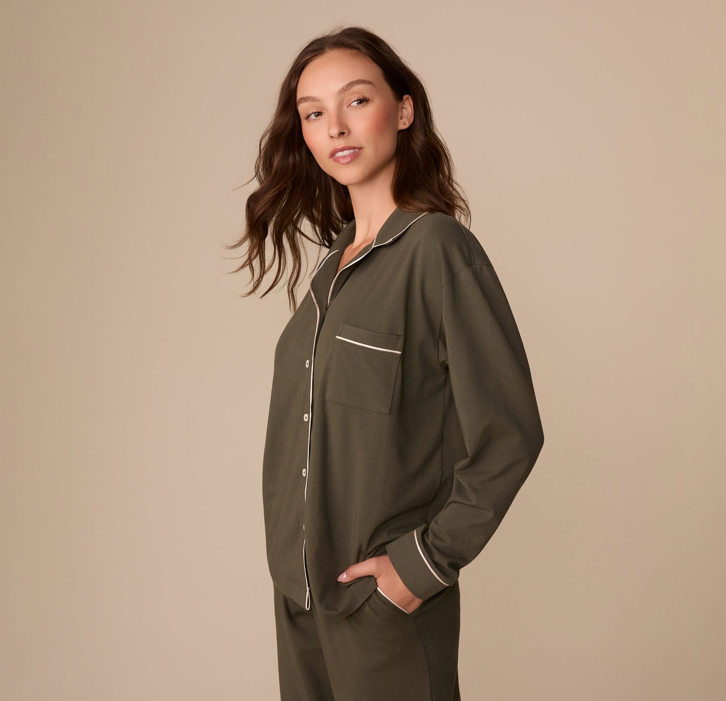 Side view of Alexis wearing the Perfect Pima Long Sleeve Pajama Shirt in Olive with her hands in her pockets. The full sleeve length and draped fit are visible.