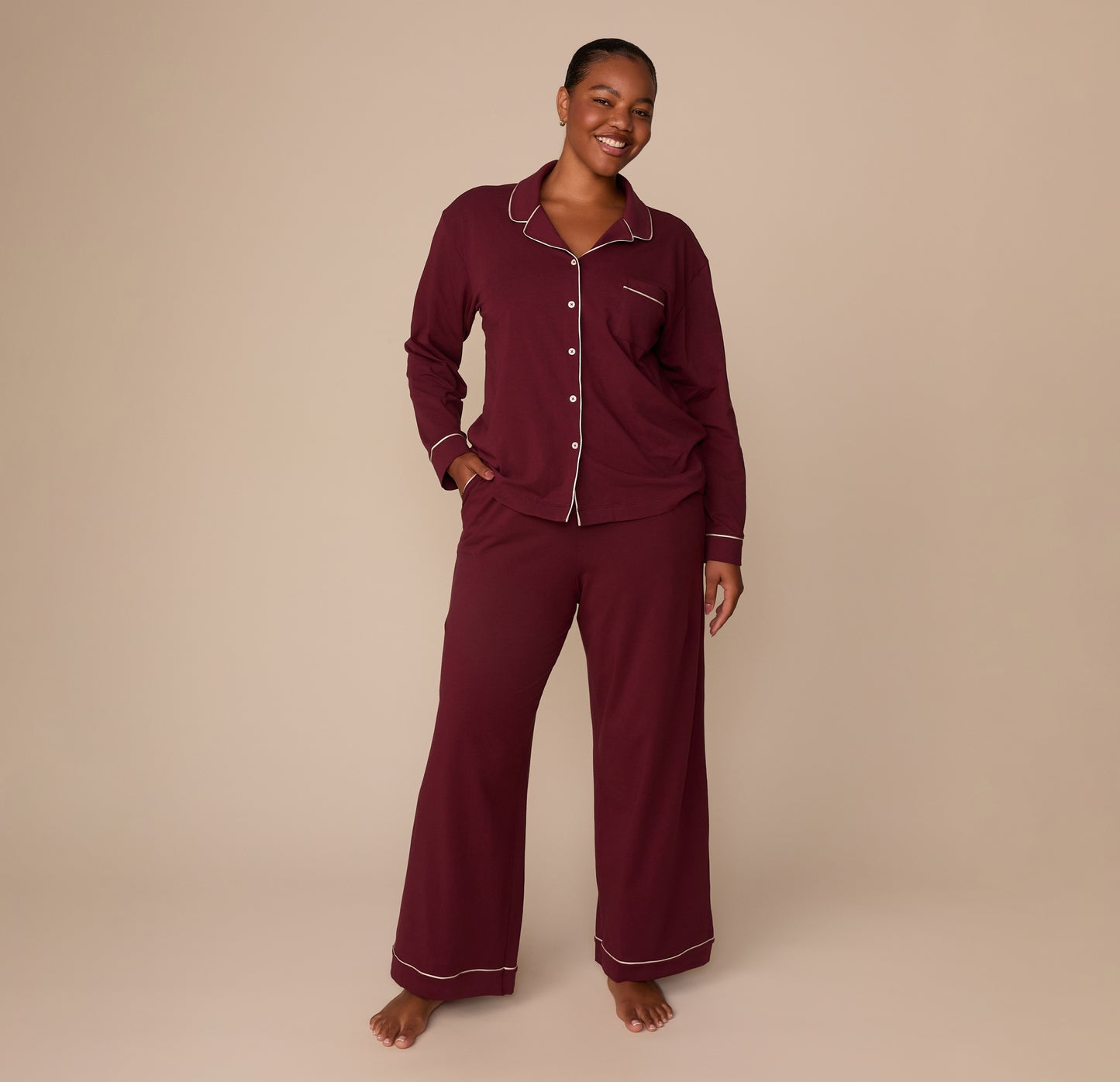 Full-body image of model Zarria in the Perfect Pima Long Sleeve Pajama Shirt and Pants in Bordeaux. She smiles with hands in pockets, showcasing the coordinated set’s comfort and fit. sizing: Zarria wears size XL
