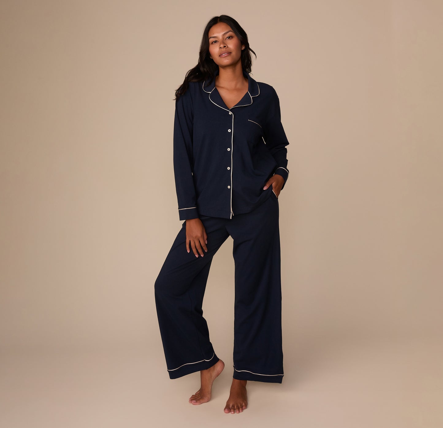 Full-body image of Victoria wearing the Perfect Pima Pajama Pants and matching Perfect Pima Long Sleeve Pajama Shirt in Navy, with her hands in the pants' side pockets and a relaxed expression.