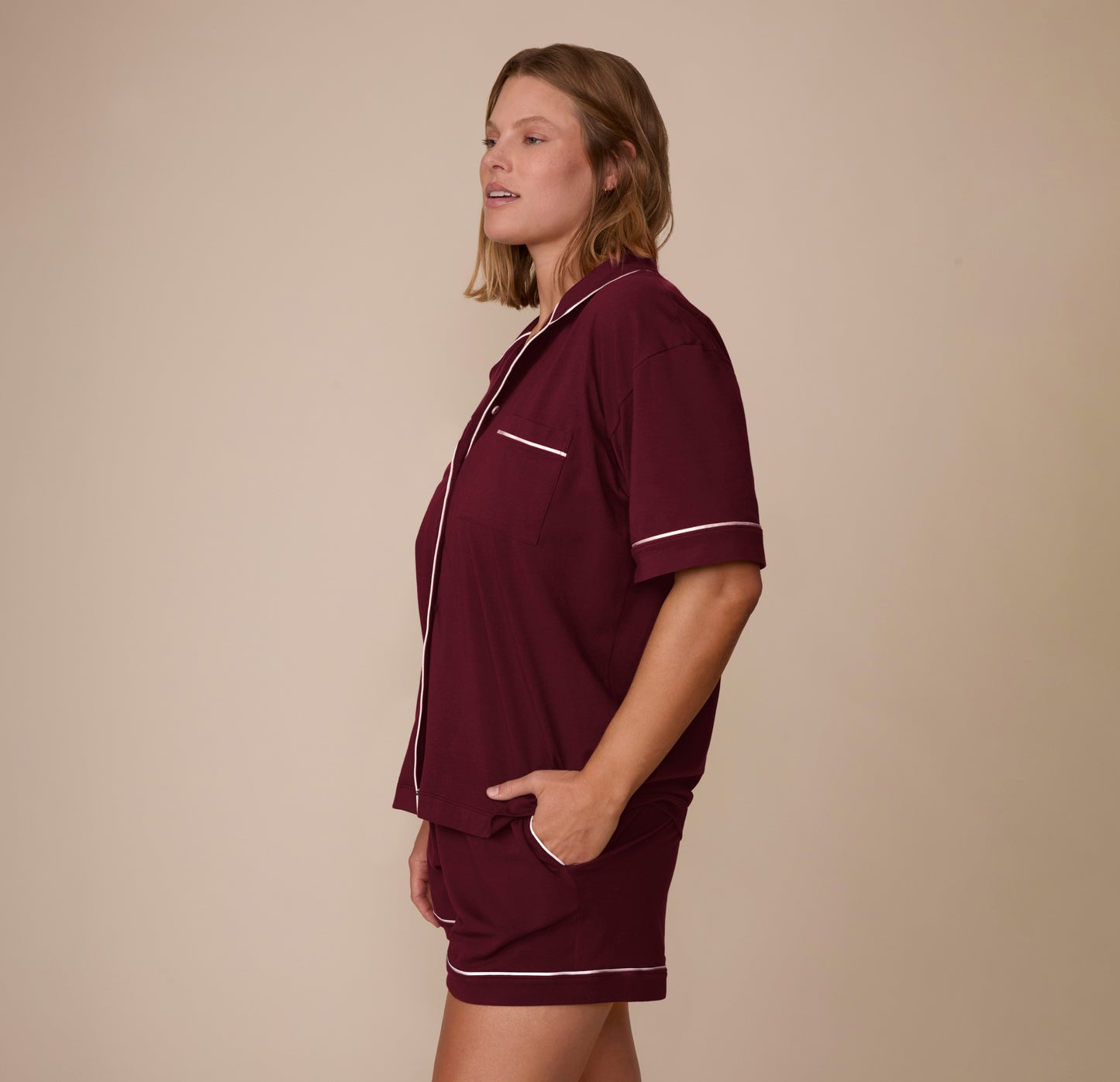 Side view of model Sonnie wearing the Perfect Pima Pajama Shirt and Shorts in Bordeaux, with one hand in the pocket of the shorts. The short-sleeve top and curved hem offer a comfy, casual silhouette.
