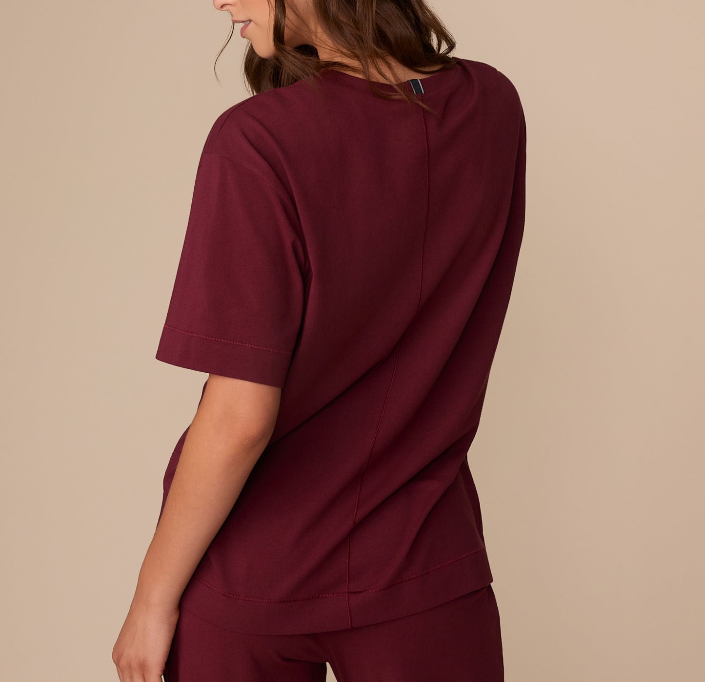 Back view of model Alexis in the Perfect Pima Pajama Tee and Pants in Bordeaux. The tee has a center back seam and a gently curved hem.