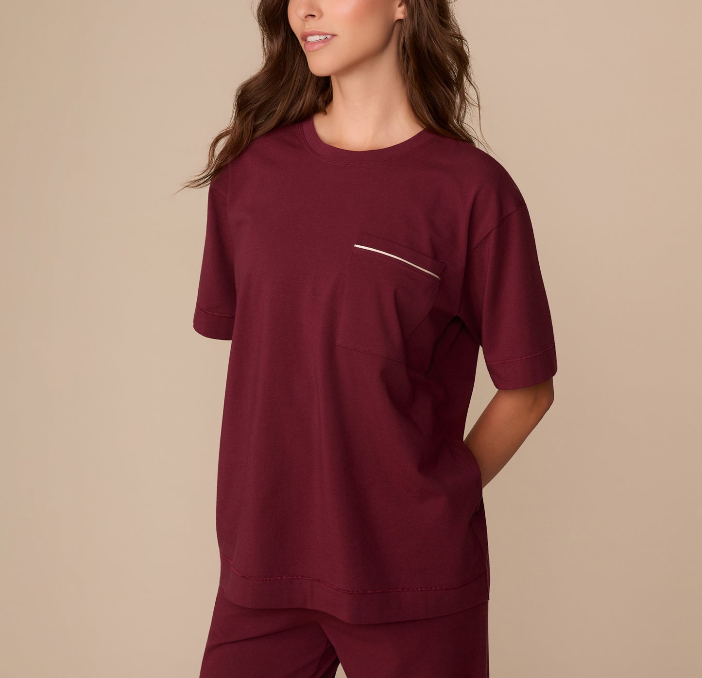 Side view of Alexis wearing the Perfect Pima Pajama Tee in Bordeaux. Her hands are tucked into her pants pockets, showcasing the drape of the tee.