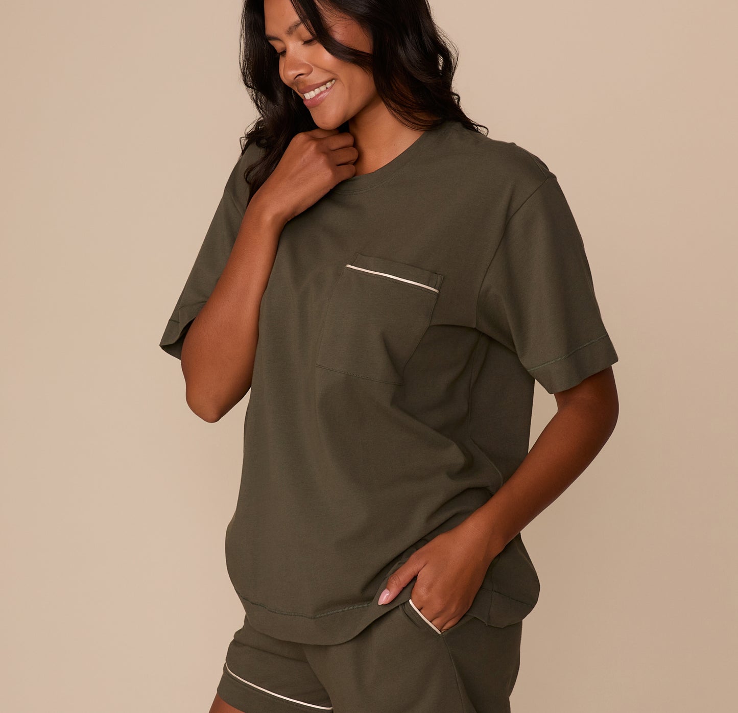Side angle of Victoria wearing the Perfect Pima Pajama Tee and Shorts in Olive. She smiles with one hand on her collar and the other in her pocket, showing the soft, easy fit.