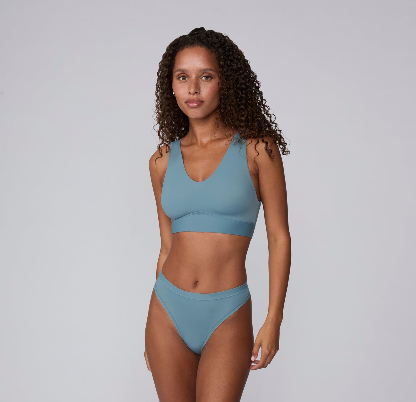 On a light studio backdrop, Courtney wears the Bliss Bralette in Poolside with the matching brief, shown in a full-body front view highlighting the scoop neckline, wide straps, smooth microfiber fabric, and wireless band designed for comfortable everyday wear.