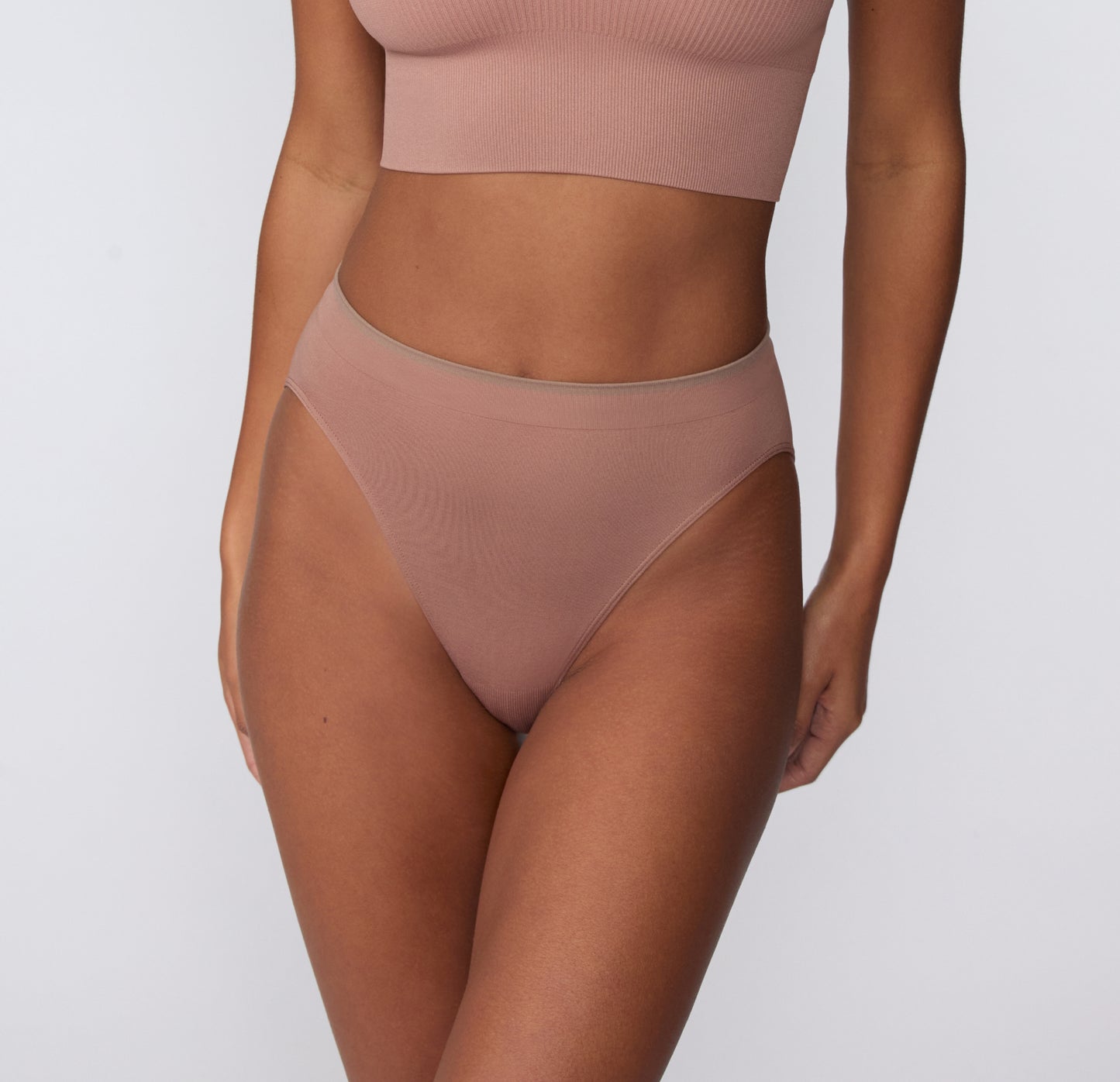 On a light gray studio backdrop, a front close-up of Courtney wearing the Smooth Seamless Brief in Plum highlights the soft microfiber fabric and flat waistband designed to sit smoothly.