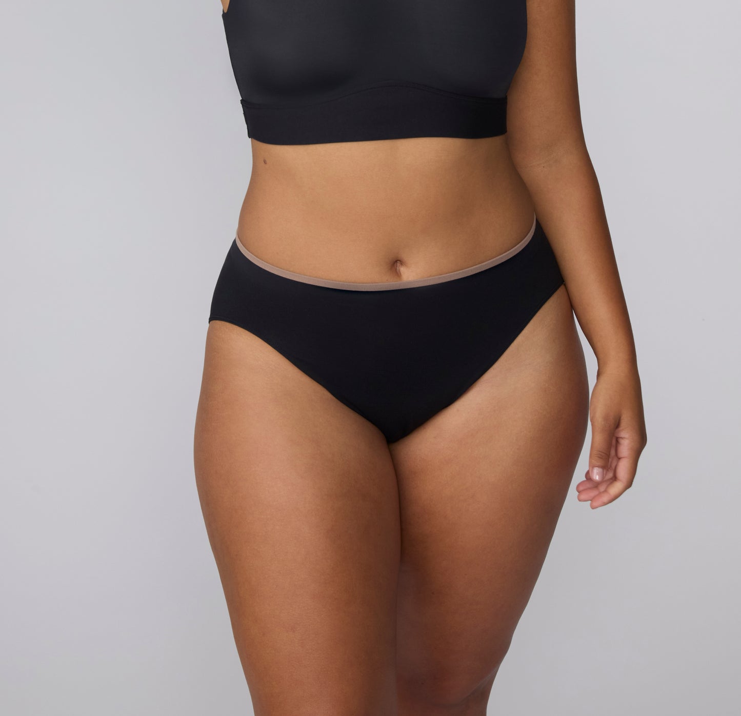 On a light gray studio backdrop, a front close-up of India wearing the Smooth Seamless underwear in Black highlights the soft microfiber fabric and flat waistband designed to sit smoothly.
