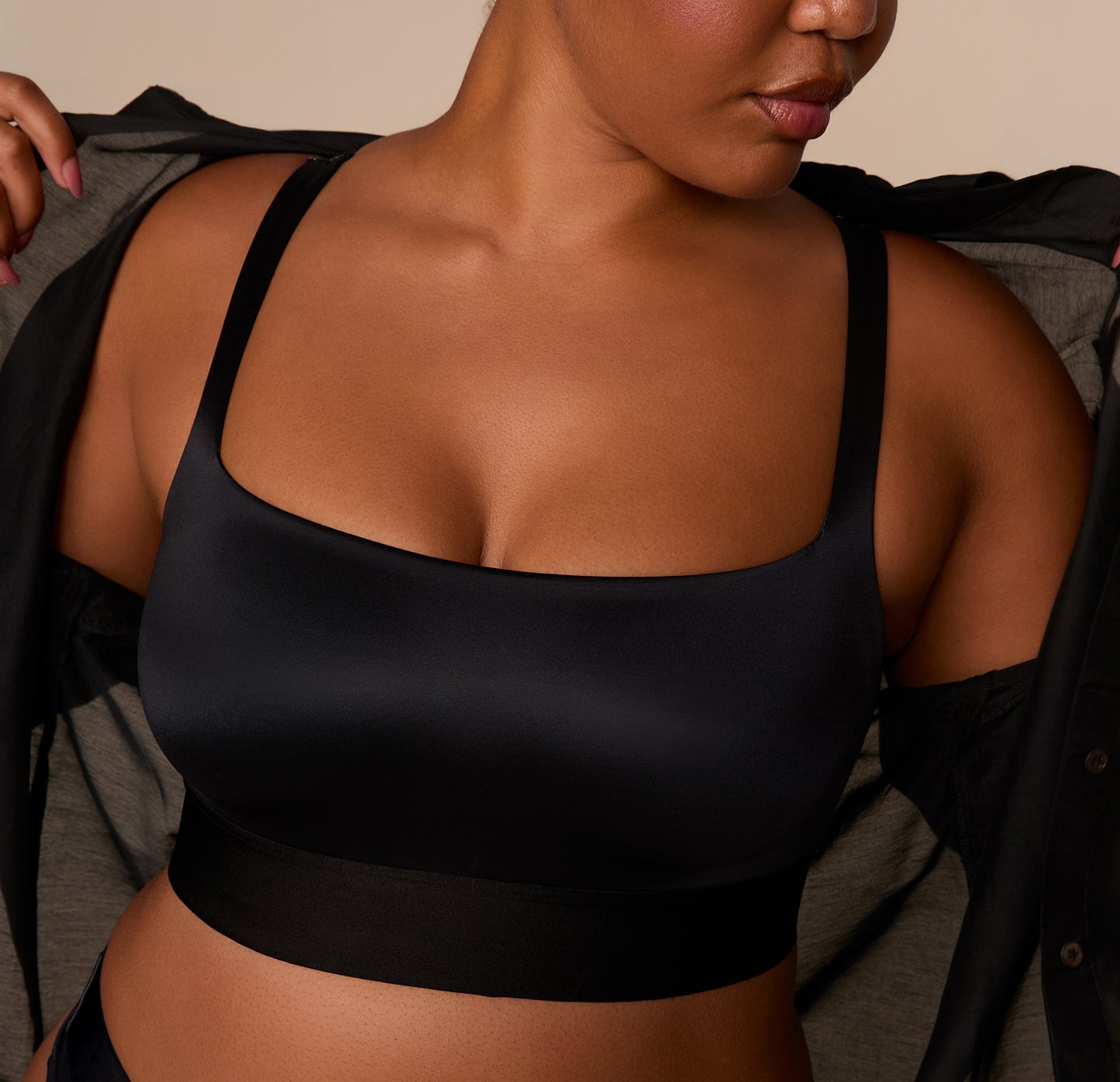 Close-up of Zarria putting on a shirt over the Stretch Satin Square Neck Bralette in Black, highlighting the sleek silhouette and supportive design.