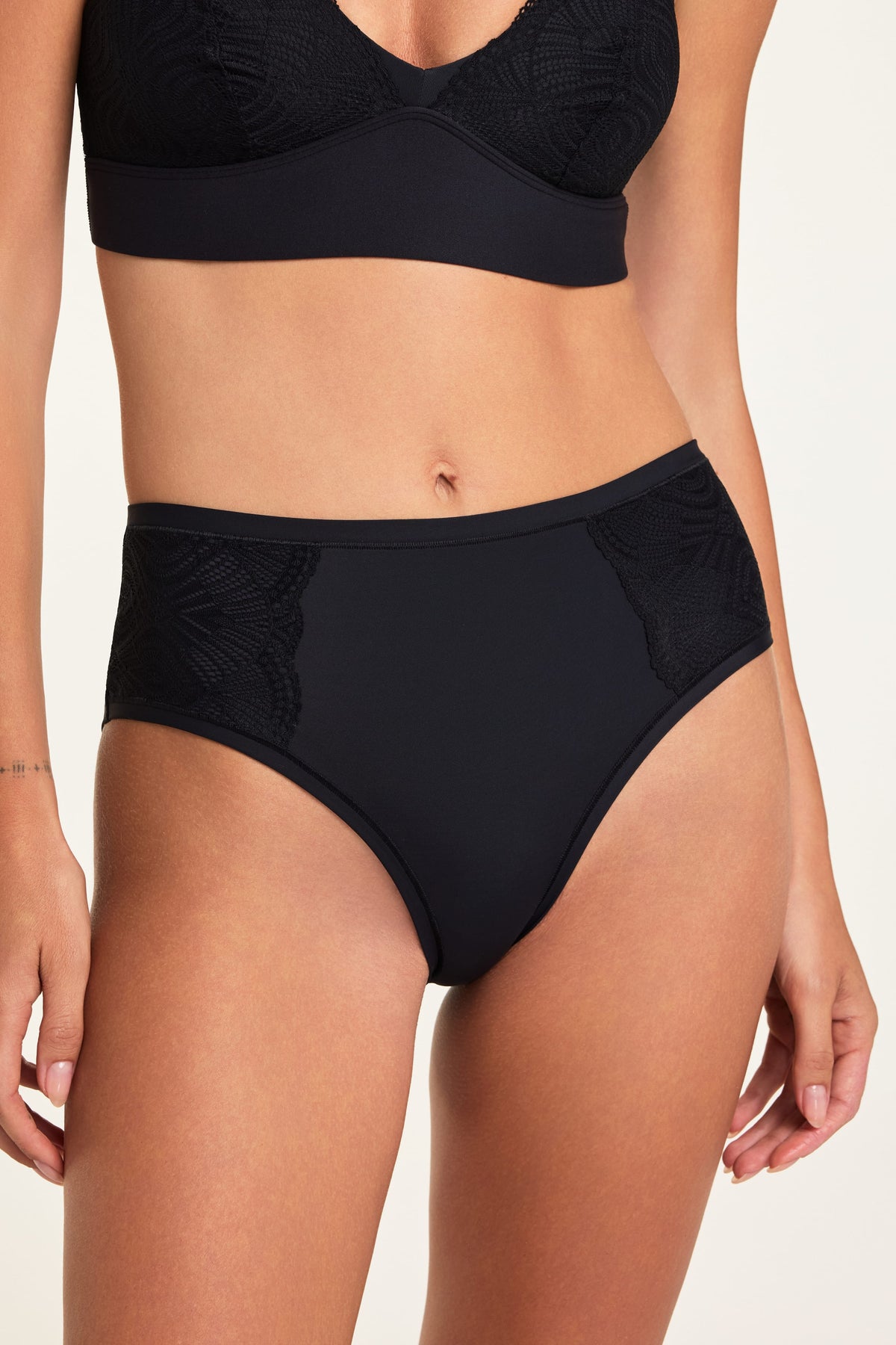 In a studio setting, Holly wears the Bliss Lace Bralette and Bliss Lace Highwaist Brief in Black, showing the V-neck bralette and high-waisted brief with soft lace trim. sizing: Holly wears size Small