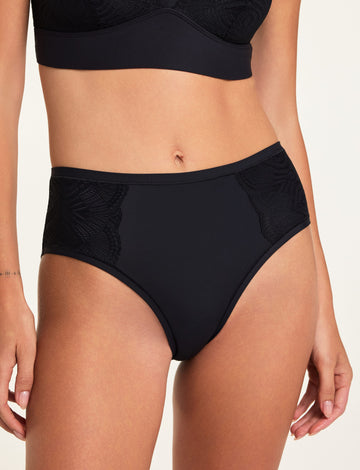 In a studio setting, Holly wears the Bliss Lace Bralette and Bliss Lace Highwaist Brief in Black, showing the V-neck bralette and high-waisted brief with soft lace trim. sizing: Holly wears size Small