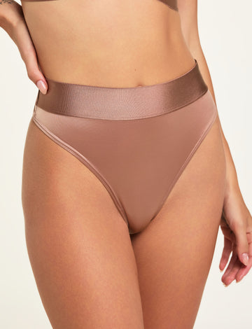On a light studio backdrop, Holly wears the Stretch Satin Highwaist Thong in Champagne, showing the silky satin fabric, high waist, and wide waistband. sizing: Holly wears size Small
