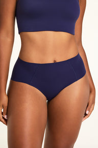 On a warm white studio backdrop, Amber wears the Whipped Knit V-Neck and No-Show Highwaist Brief in Noir, showing the brief’s high waist and front seam details. sizing: Amber wears size Large