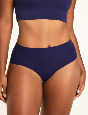 On a warm white studio backdrop, Amber wears the Whipped Knit V-Neck and No-Show Highwaist Brief in Noir, showing the brief’s high waist and front seam details. sizing: Amber wears size Large