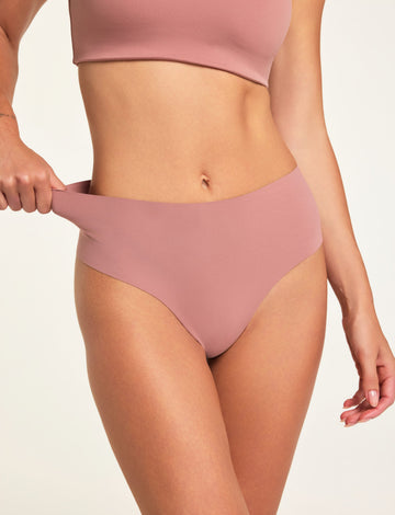 In a studio setting, Holly wears the Whipped Knit V-Neck in Plum and No-Show Highwaist Thong in Plum, pulling the thong waistband to show its stretch. sizing: Holly wears size Small 
