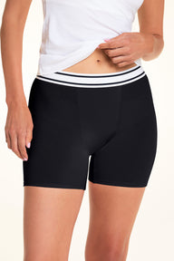 A close-up of Meagan wearing the Cloud Cotton Boxer Brief in Black, paired with a white camisole. The front view highlights the striped waistband, smooth fabric, and fitted mid-thigh silhouette. sizing: Meagan wears size Small