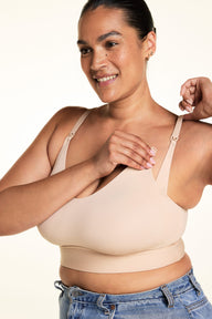 Jennifer wears the Bliss Nursing Bralette in Beige against a warm white studio backdrop, holding the nursing clip at the neckline to show the nursing access feature and adjustable shoulder straps. sizing: Jennifer wears size XL 