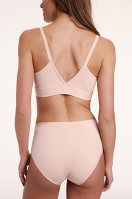 On a light studio backdrop, Gianna wears the Bliss Triangle Bralette in Rose, shown from the back. The bralette features a V-shaped back, adjustable straps, and a smooth underband.