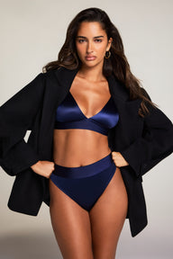 In a studio setting, Kushi wears the Stretch Satin Triangle Bralette and Stretch Satin Highwaist Thong in Navy, layered under a black blazer. The bralette features a deep V-neck and adjustable strap