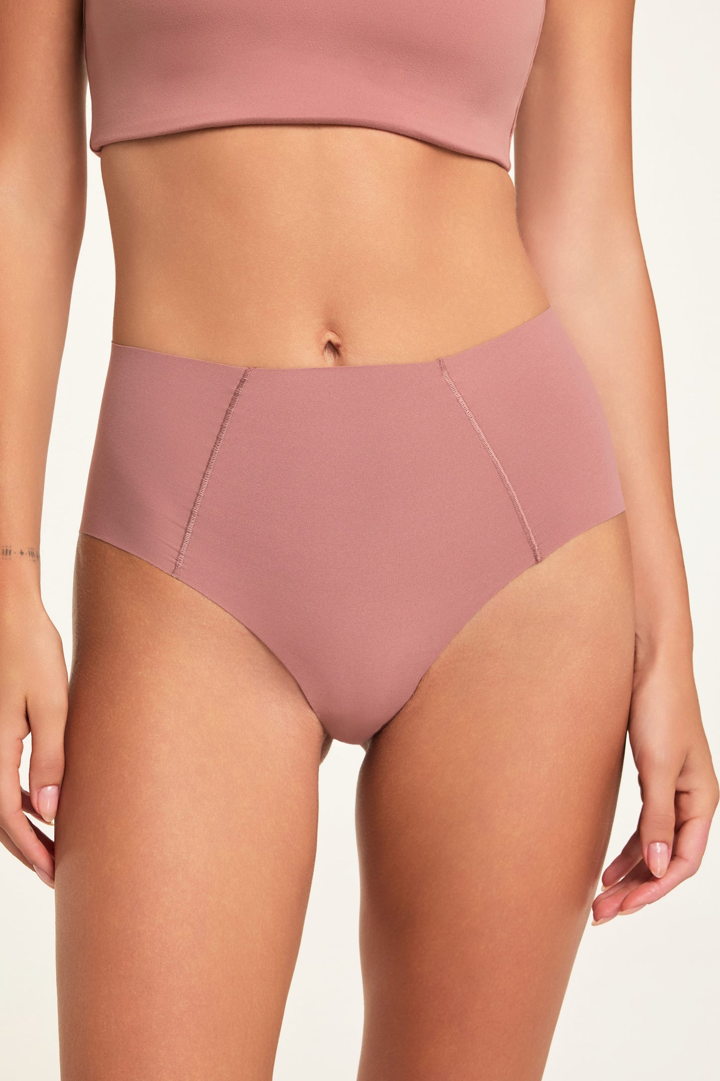 In a studio setting, Holly wears the Whipped Knit No-Show Highwaist Brief in Plum, shown in a close-up front view to highlight the high-waisted cut and angled seam details.