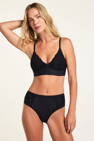 On a warm white studio backdrop, Holly wears the Bliss Lace Bralette in Black and Bliss Lace Highwaist Brief in Black, showing the full set with lace-trimmed cups, a V-neckline, and high-waisted brief.