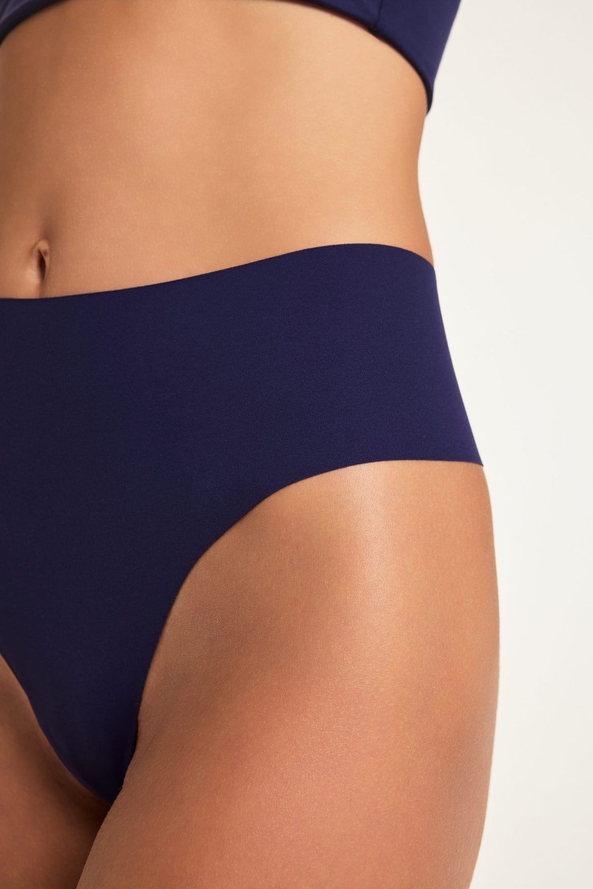 Close-up on a studio backdrop of Holly wearing the No-Show Highwaist Thong in Noir, highlighting the high-waisted front and smooth fabric.