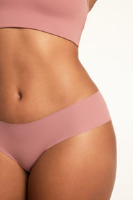On a white studio backdrop, Amber wears the WhippedKnit Scoop and No-Show Hiphugger in Plum, shown from the side to highlight the Hiphugger’s waistband and coverage.