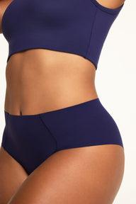 Close-up on a warm white studio backdrop of Amber wearing the No-Show Highwaist Brief in Noir, showing the high waist and curved front seam details.