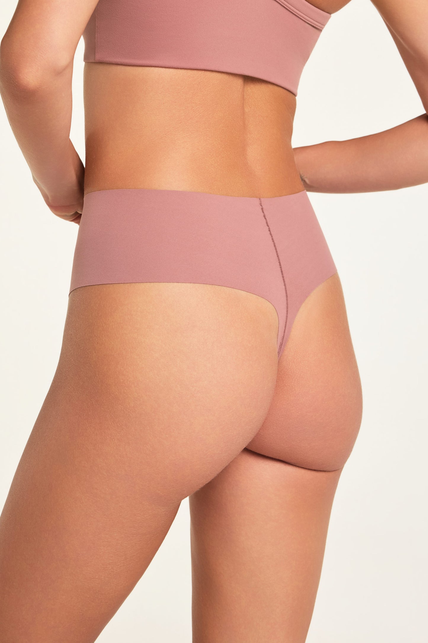 On a light studio backdrop, Holly wears the Whipped Knit V-Neck and No-Show Highwaist Thong in Plum, shown from the back.