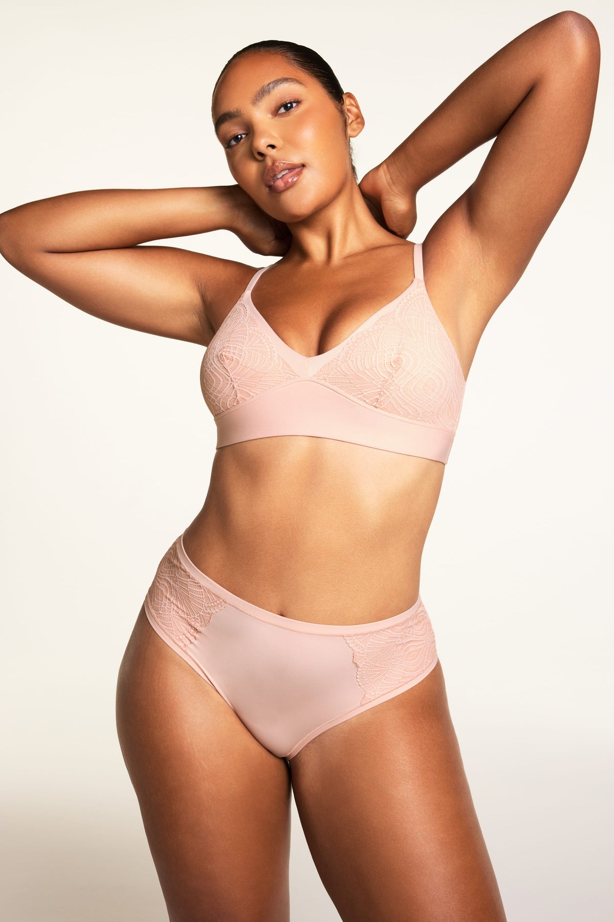 On a warm white studio backdrop, Amber wears the Bliss Lace Bralette in Ember Rose and Bliss Lace Highwaist Brief in Ember Rose, showing the full set with lace-trimmed V-neck bralette, wireless band, and high-waisted brief with lace detailing.
