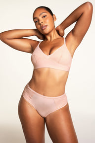 On a warm white studio backdrop, Amber wears the Bliss Lace Bralette in Ember Rose and Bliss Lace Highwaist Brief in Ember Rose, showing the full set with lace-trimmed V-neck bralette, wireless band, and high-waisted brief with lace detailing.