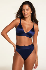 On a light studio backdrop, Kushi wears the Stretch Satin Triangle Bralette and Stretch Satin Highwaist Thong in Navy, showing the matching set with a deep V-neck, adjustable straps, and wide waistbands.