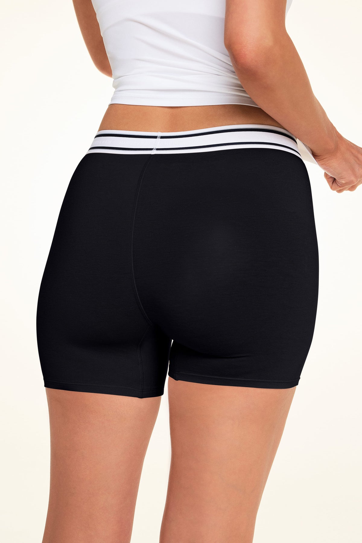 Meagan is shown from behind wearing the Cloud Cotton Boxer Brief in Black. The close-up highlights the smooth back panel, fitted leg openings, and white waistband with black stripes.