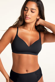 A close-up of a model wearing a black V-neck bra with adjustable straps and matching black underwear with lace side panels, highlighting the smooth fabric and delicate detailing.