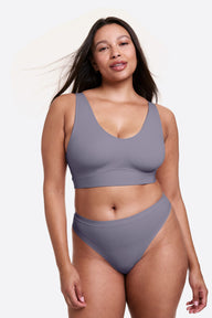 On a white studio backdrop, Alana wears the Bliss Bralette in Steel with matching underwear, standing facing forward. The bralette features a deep V-neck, wide straps, and a supportive underband.  sizing: Alana wears size Large