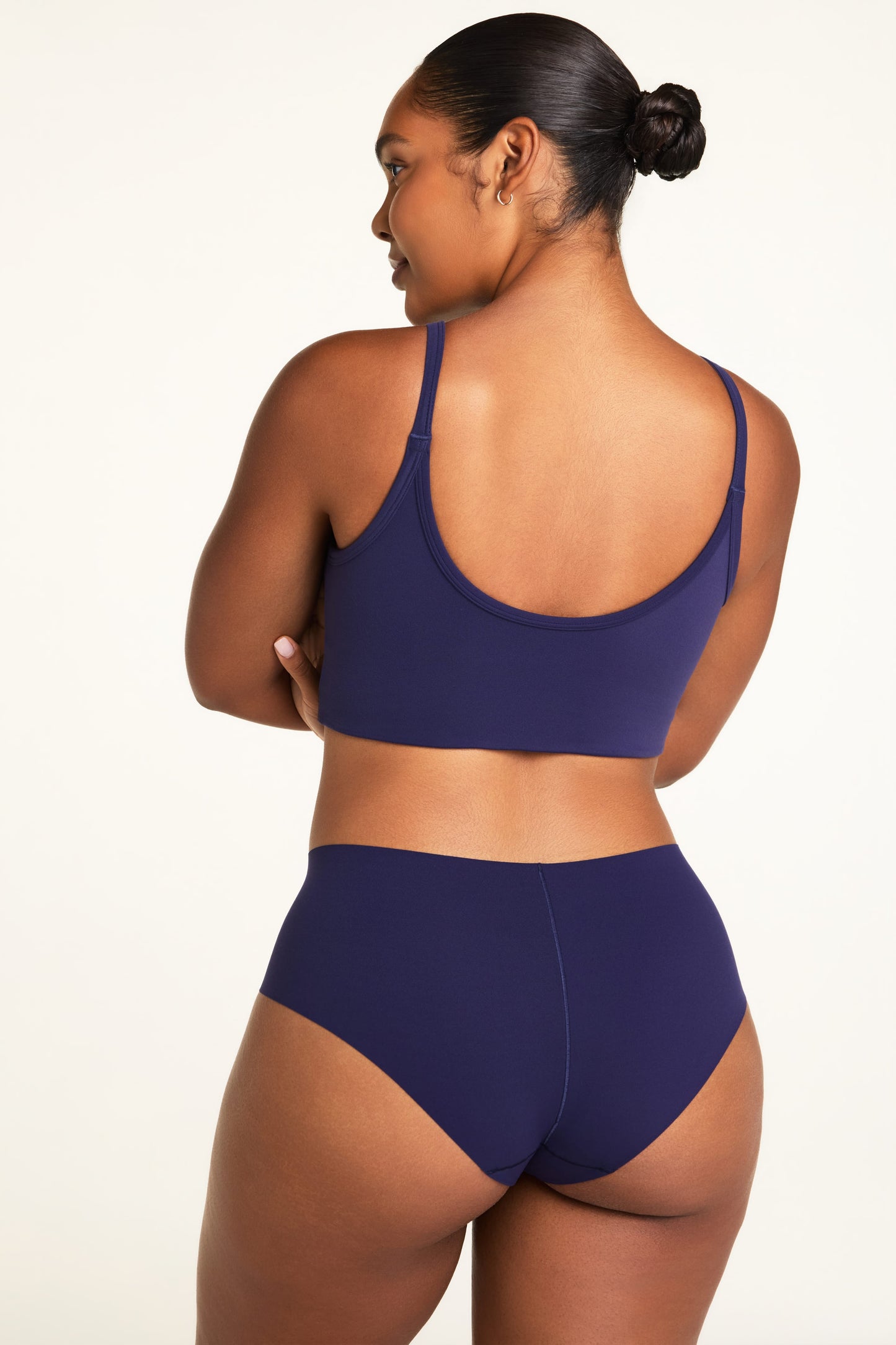 On a warm white studio backdrop, Amber wears the Whipped Knit V-Neck and No-Show Highwaist Brief in Noir, shown from the back to highlight the top’s scoop back and the brief’s full back coverage.