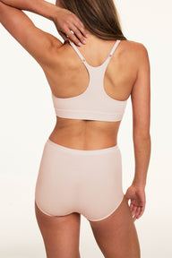 Against a warm white studio backdrop, Gianna models the Bliss Racerback Bralette and Bliss Boyshort in Cabana, shown from behind. The bralette features a racerback design with adjustable straps and a wide underband, while the matching boyshorts have a high-rise waistband and full back coverage.