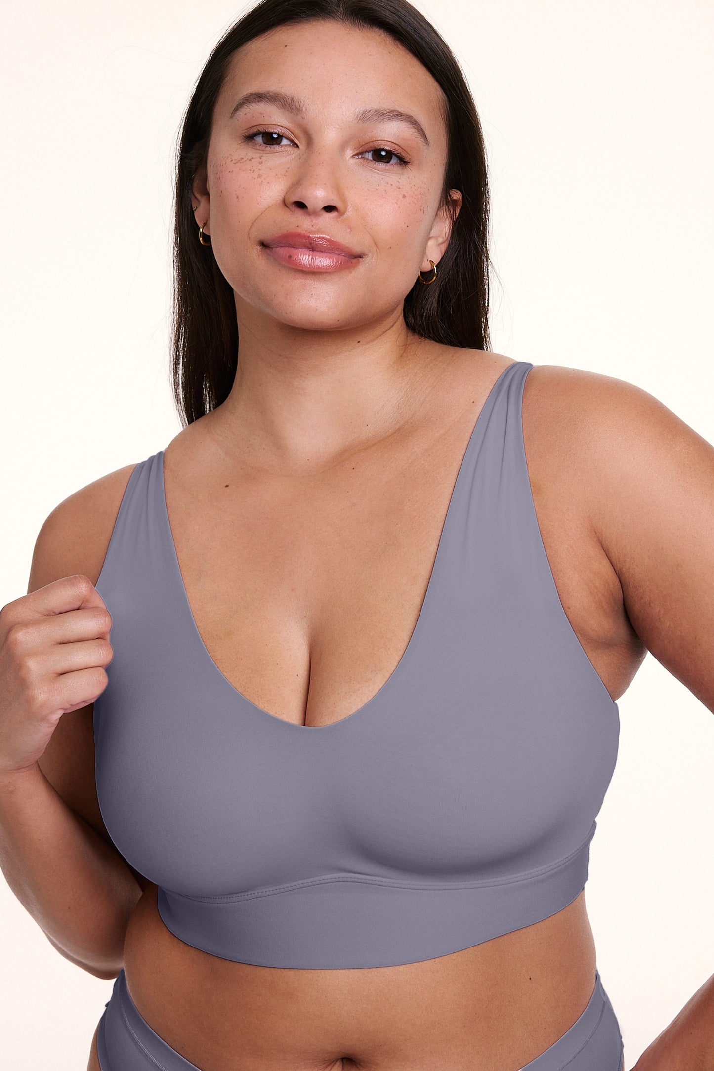 On a white studio backdrop, Alana wears the Bliss Bralette in Steel, shown in a close-up. The bralette features a deep V-neckline, wide straps, and smooth, lightweight fabric.