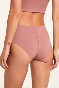In a studio setting, Holly sits wearing the Whipped Knit No-Show Highwaist Brief in Plum, offering a close-up back view of the smooth fabric and high-waisted cut.