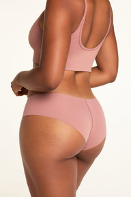 On a white studio backdrop, Amber wears the WhippedKnit Scoop and No-Show Hiphugger in Plum, shown from the back with the Scoop’s adjustable straps and Hiphugger underwear.