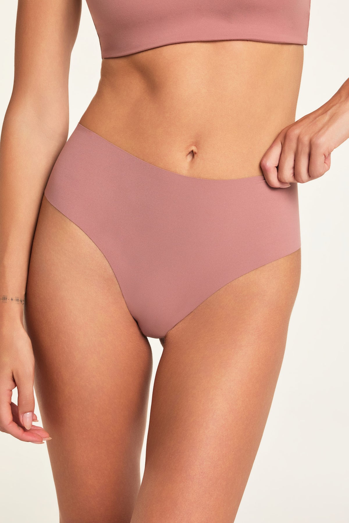 Close-up front view of Holly wearing the No-Show Highwaist Thong in Plum, with the waistband pulled slightly to show its stretch.