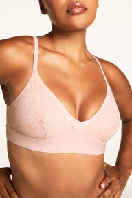 On a warm white studio backdrop, Amber wears the Bliss Lace Bralette in Ember Rose, shown in close-up to highlight the V-neckline, delicate lace trim, thin adjustable straps, and wide wireless band.