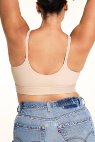 Back view of Jennifer wearing the Bliss Nursing Bralette in Beige, showing the low scoop back, adjustable shoulder straps, and wide underband against a warm white studio backdrop.