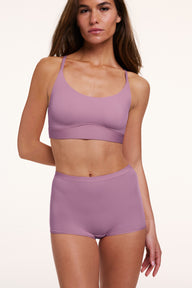 In a studio setting, a model wears the Bliss Boyshort in Mirage with a matching bra, shown in a front-facing pose. The design features a mid-rise waistband, full coverage, and a smooth, seamless finish. sizing: Gianna wears size Small