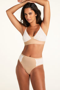 In a bright studio, Kushi wears the Bliss Lace Bralette and Bliss Lace Highwaist Brief in Beige, showing the V-neck bralette and lace-trimmed high-waisted brief from the front.
