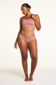 On a white studio backdrop, Amber wears the WhippedKnit Scoop and No-Show Hiphugger in Plum, shown in a full-length front view.