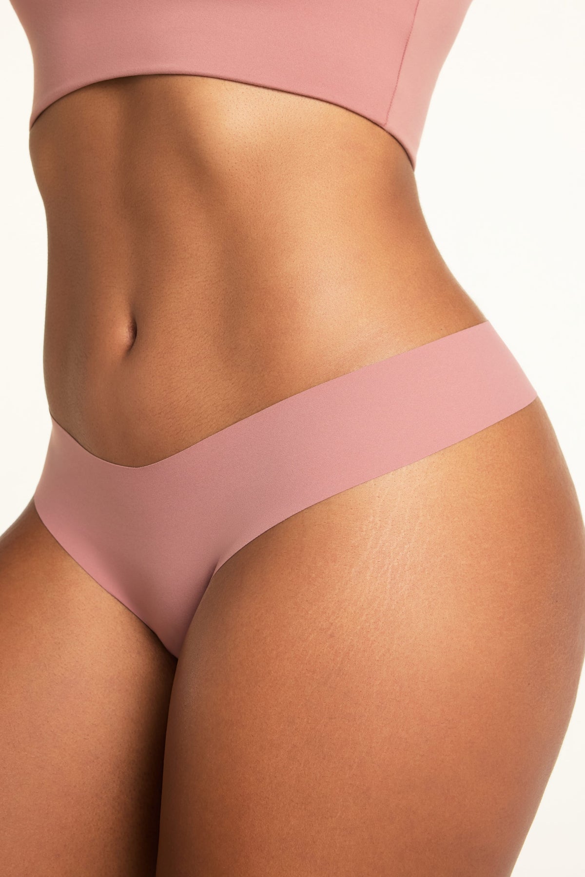 On a white studio backdrop, close-up of Amber wearing the No-Show Low-Rise Thong in Plum, showing the smooth, wide waistband and low-rise cut.