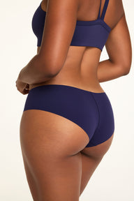 On a white studio backdrop, Amber wears the WhippedKnit V-Neck and No-Show Hiphugger in Noir from the back, showing the bra’s straps and the Hiphugger’s back coverage.