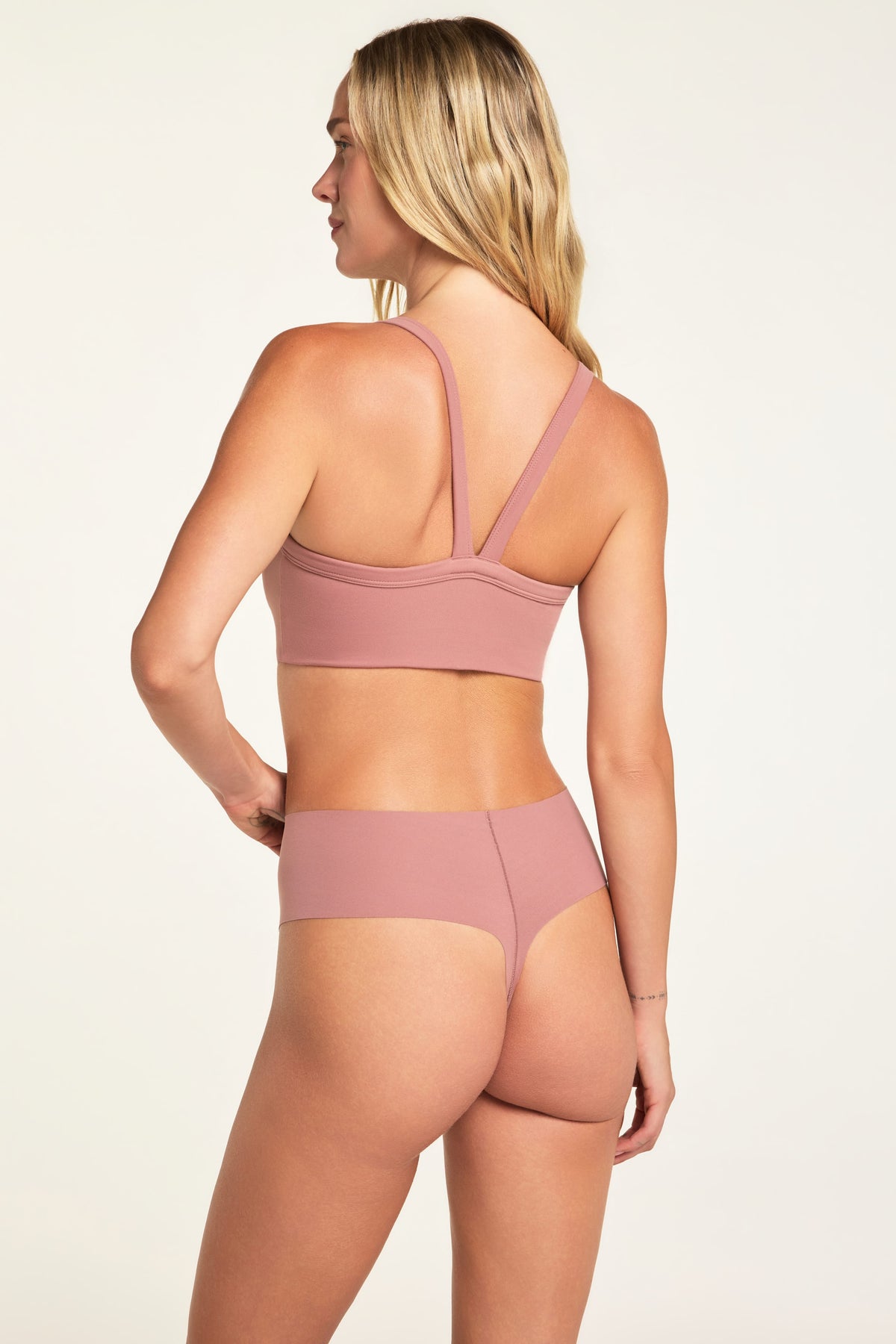 On a light studio backdrop, Holly wears the Whipped Knit V-Neck in Plum and No-Show Highwaist Thong in Plum, shown from the back while the thong has a high-rise waistband and minimal back coverage.