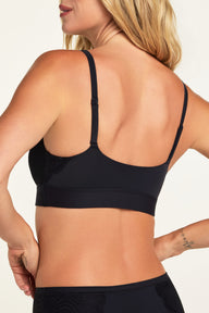 On a warm white studio backdrop, Holly wears the Bliss Lace Bralette in Black and Bliss Lace Highwaist Brief in Black, shown from the back to highlight the bralette’s V-back, adjustable straps, wide band, and lace panels on the brief.