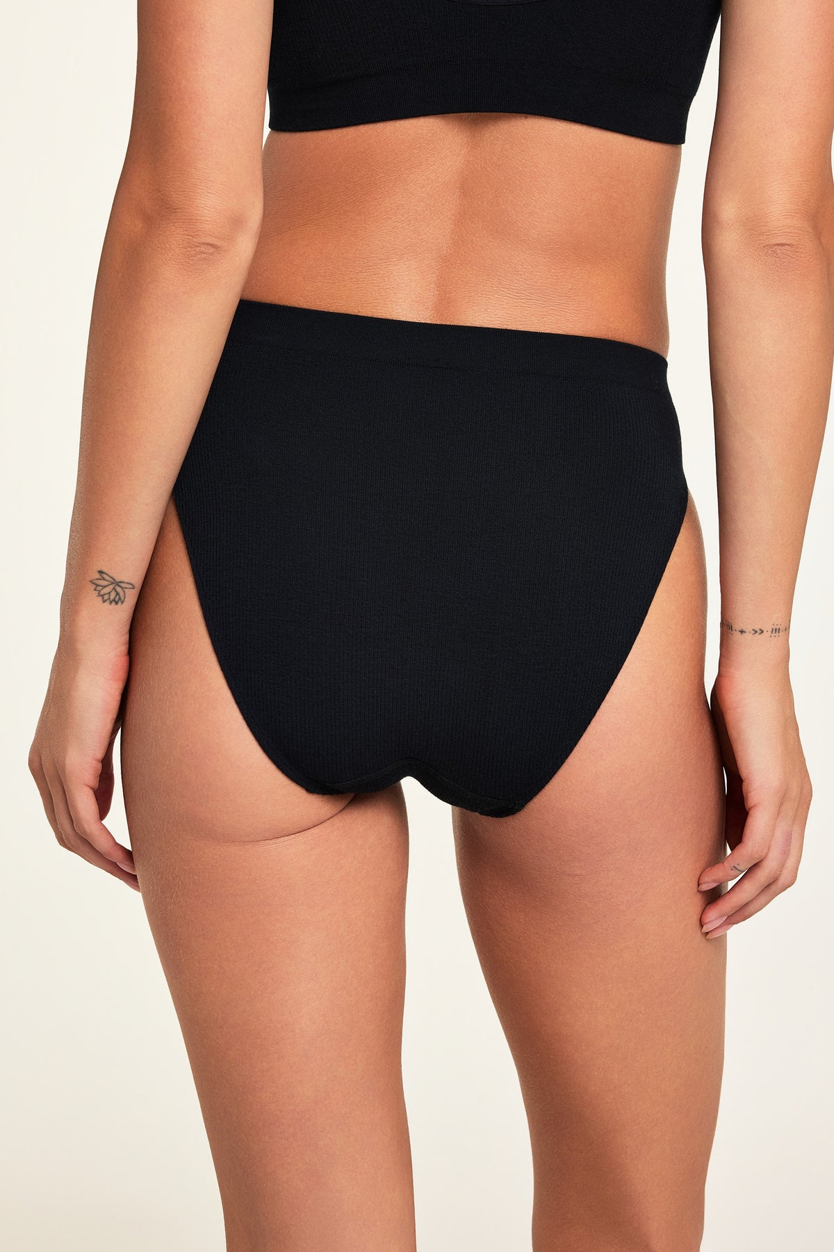 Three-quarter back view of the Knit Seamless French Cut Brief in Black paired with the Knit Seamless Bralette in Black.